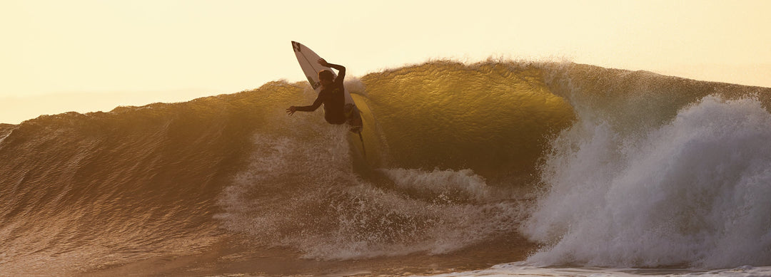 Surfer jumping out of a wave at sunset