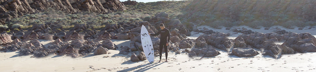 Mana with surfboard in front of rocks